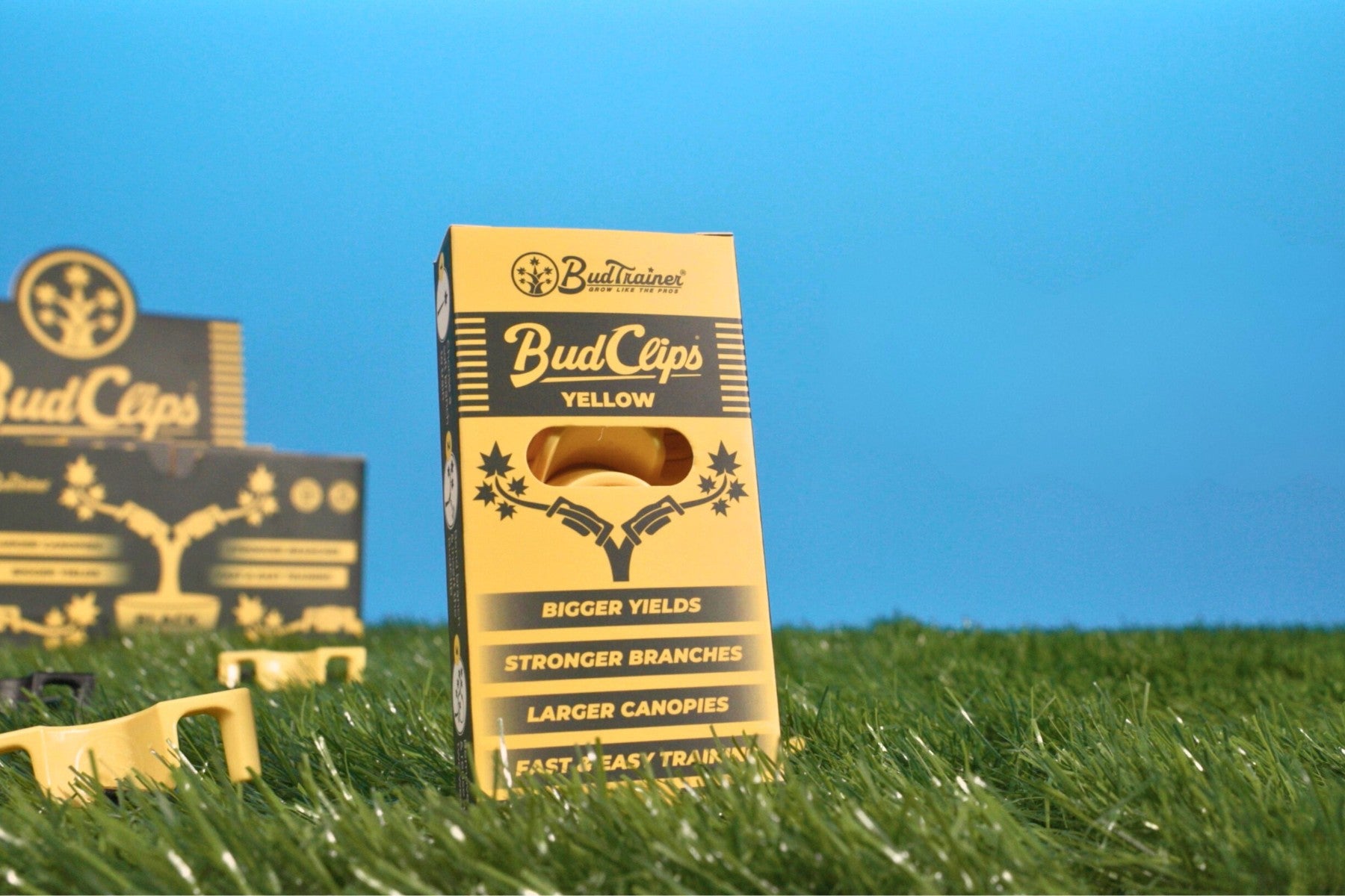BudClips yellow packaging displayed on green grass with bold benefits listed, including bigger yields, stronger branches, and larger canopies.