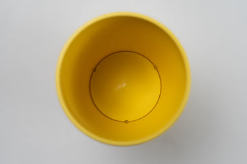 Top-down view inside a yellow BudCups container showing a small drainage hole in the center, surrounded by three circular ridges on the container's base, against a plain white background.