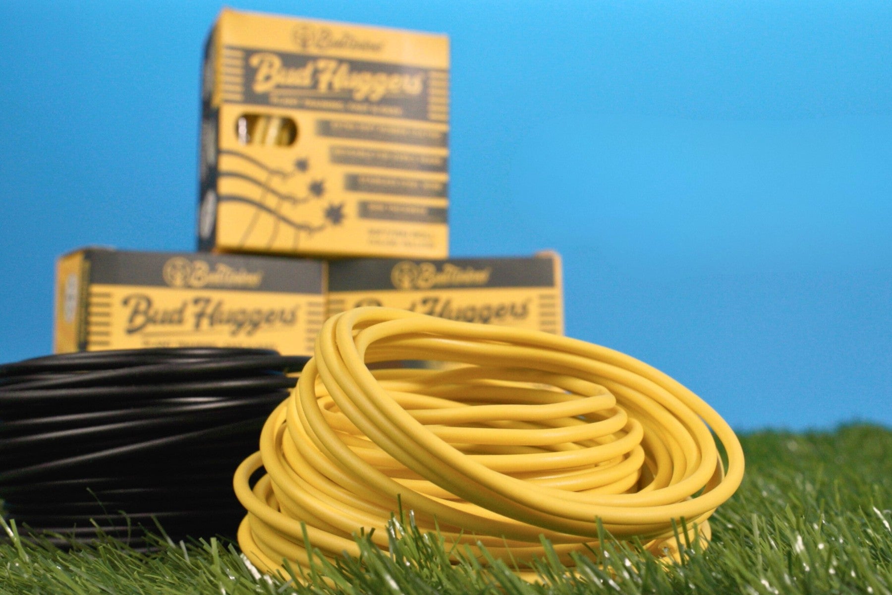 Coils of yellow and black BudHuggers plant training wire displayed in front of branded packaging boxes.