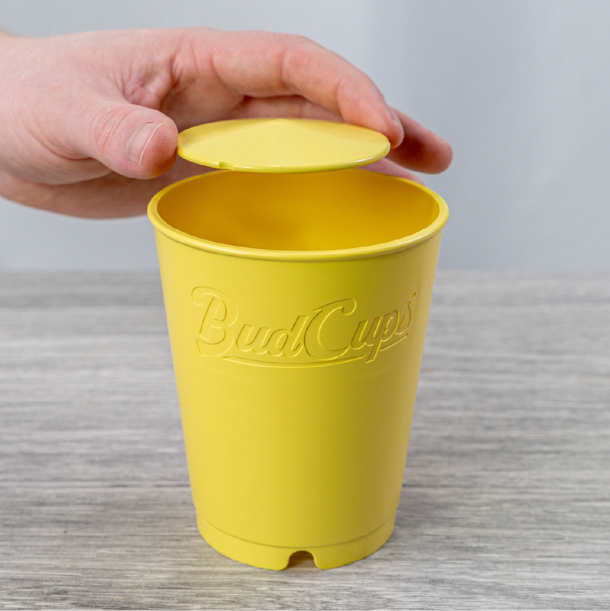 Hand opening BudTrainer BudCups reusable seed starter cup with drainage holes for cannabis seedlings.