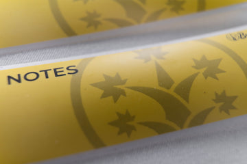 Macro shot of BudTrainer yellow sticky notes with cannabis grow logo and notes section.