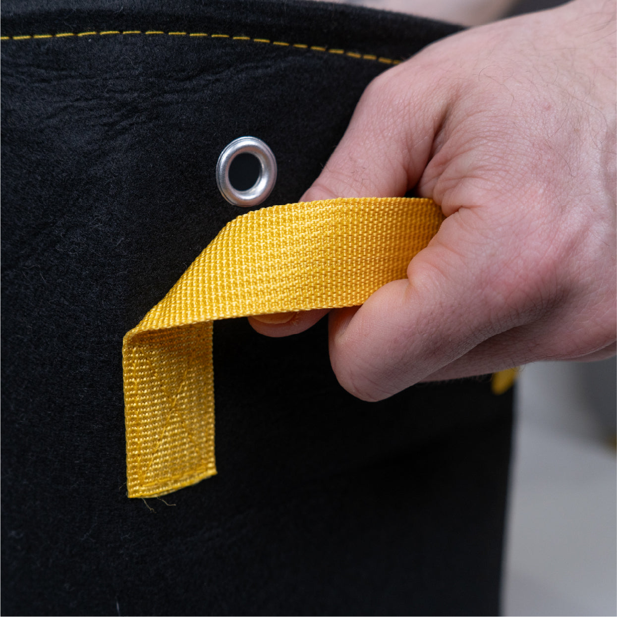 Hand holding sturdy handle of BudTrainer BudPots fabric pot for easy cannabis plant transport.