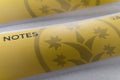 Macro shot of BudTrainer yellow sticky notes with cannabis grow logo and notes section.